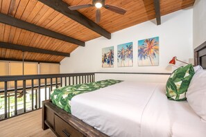 A bedroom with a bed, a ceiling fan, a nightstand, a lamp, and a balcony.