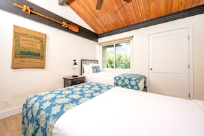 A bedroom with two beds, a window with a view, a wooden ceiling, and a wall-mounted coffee book.