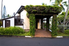 A house with a covered entrance, a small porch, and a garden with various plants and a palm tree.
