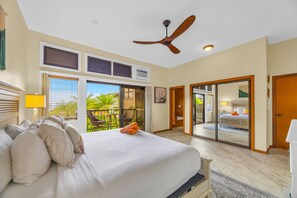 Habitación de hotel con una cama grande, ventilador de techo, puertas corredizas de vidrio a un balcón y vistas al exterior.
