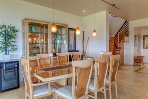 Un coin repas avec un meuble vitré, des chaises en bois, une table en verre, des luminaires suspendus et un escalier en arrière-plan.