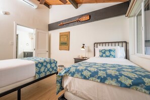 A bedroom with two beds, a nightstand, a lamp, a framed picture, and a window. - Napili Point | Oceanfront 4 BR, Sleeps 10 | Car Incl. w/ 6+ Nights | NAP ML-1175 by KBM (Lahaina)