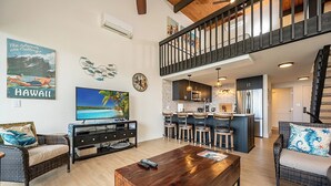 A spacious living area with a large TV, a wooden coffee table, and a kitchen with bar stools. - Napili Point | Oceanfront 4 BR, Sleeps 10 | Car Incl. w/ 6+ Nights | NAP ML-1175 by KBM (Lahaina)