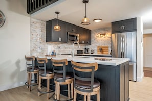 Una cocina moderna con una isla central, taburetes de bar, armarios oscuros y electrodomésticos de acero inoxidable.