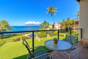 A balcony with a view of the ocean, a pool, and a lawn.