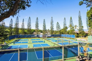 Un complejo de canchas de tenis con varias pistas, rodeado de árboles altos y un cielo despejado.
