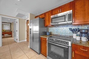 A kitchen with stainless steel appliances, wooden cabinets, a tiled backsplash, and a countertop with kitchen utensils. - Honua Kai | Ocean View 4 BR, Sleeps 12 | Car Incl. w/ 6+ Nights | HKK ML-1183 by KBM (Lahaina)