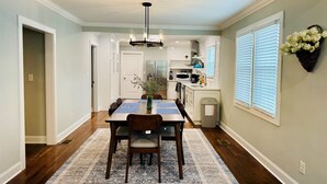 A dining area with a wooden table and chairs, a vase with flowers, and a kitchen in the background. - NEW! 3BR/2BA home in the heart of Spartanburg SC! (Spartanburg)