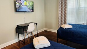 A hotel room with a bed, a desk with a chair, a TV on the wall, and a window with curtains. - NEW! 3BR/2BA home in the heart of Spartanburg SC! (Spartanburg)