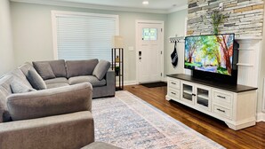 A living room with a grey sofa, a flat-screen TV on a white cabinet, a patterned rug, and a stone wall. - NEW! 3BR/2BA home in the heart of Spartanburg SC! (Spartanburg)