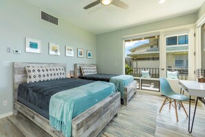 A bedroom with a large bed, a smaller bed, a desk, and a chair. There are multiple framed pictures on the wall.