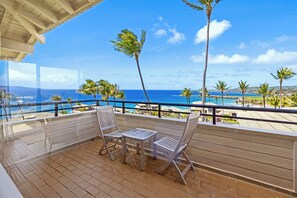 Un balcón con vista al océano, palmeras y una terraza de madera.