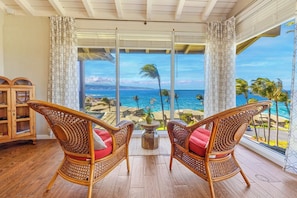Una habitación con dos sillones de mimbre, un armario de madera y un ventanal con vistas al océano y palmeras.