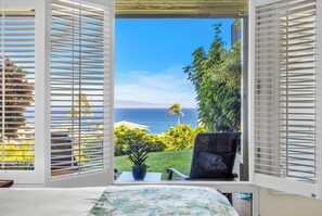 A bedroom with a view of the ocean, a chair, and a small table.