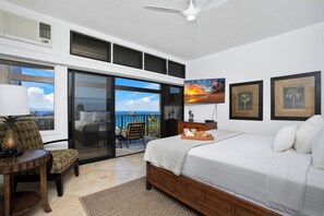 A bedroom with a large bed, a desk with a lamp, a chair, and a view of the ocean through a sliding door. - Kapalua Ridge | Ocean View 3 BR, Sleeps 10 | Car Incl. w/ 6+ Nights | KRV ML-1197 by KBM (Lahaina)