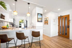 Una cocina moderna con una isla central, taburetes de bar, iluminación colgante y una puerta de madera.