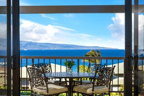 Un balcón con mesa y sillas, con vistas a la costa, montañas y el mar.
