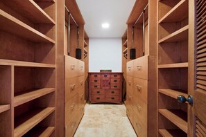 A walk-in closet with wooden shelving and drawers, a tiled floor, and a small cabinet in the center. - Kapalua Ridge | Ocean View 3 BR, Sleeps 10 | Car Incl. w/ 6+ Nights | KRV ML-1197 by KBM (Lahaina)
