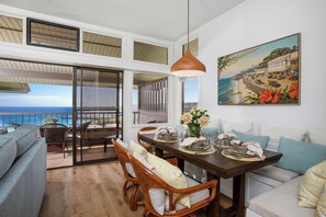 A dining area with a view of the ocean, a painting of a coastal scene, and a balcony with a view. - Kapalua Ridge | Ocean View 3 BR, Sleeps 10 | Car Incl. w/ 6+ Nights | KRV ML-1197 by KBM (Lahaina)