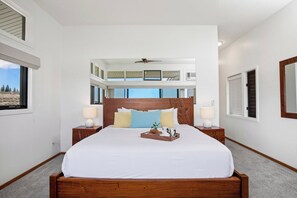 A bedroom with a large bed, two bedside tables, a ceiling fan, and a view of the outdoors.