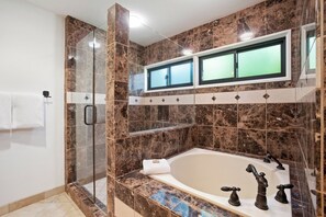 Une salle de bain avec une douche à parois de verre, une baignoire dotée de deux robinets et un miroir au-dessus de la baignoire.