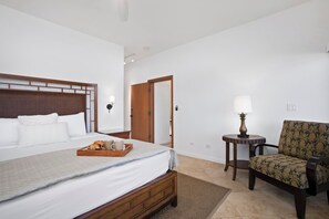 A hotel room with a bed, bedside table, chair, and a small table with a lamp. - Kapalua Ridge | Ocean View 3 BR, Sleeps 10 | Car Incl. w/ 6+ Nights | KRV ML-1197 by KBM (Lahaina)