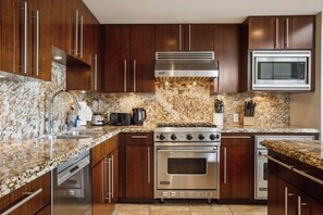 A kitchen with dark wood cabinets, a stainless steel stove, a microwave, and granite countertops.