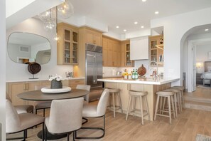 A modern kitchen with a central island, wooden cabinets, and a dining area with chairs.