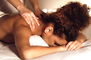 Eine Person liegt auf einem Bett mit einem Handtuch, die Hand einer anderen Person berührt ihren Kopf.