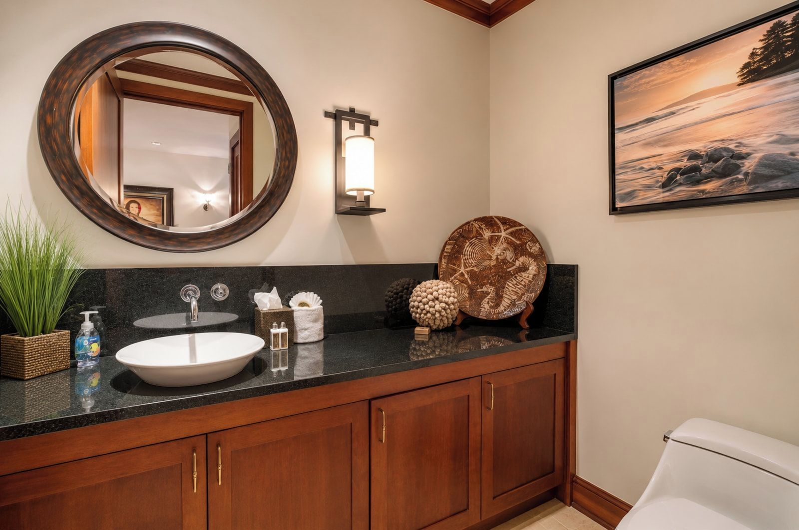 A bathroom with a round mirror, a sink, a wall-mounted light, a framed picture, and wooden cabinets.
