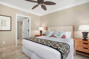 A hotel room with a bed, two bedside tables, a ceiling fan, and a door leading to another room. - Honua Kai | Ocean View 5 BR, Sleeps 14 | Car Incl. w/ 6+ Nights | HKH ML-1235 by KBM (Lahaina)