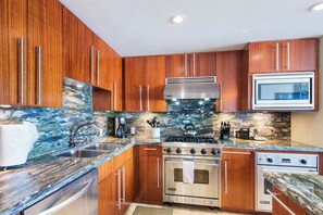 A kitchen with wooden cabinets, a stainless steel stove, and a microwave. - 2 Honua Kai Villas | Ocean Front | Sleeps 14 | Free Car w/ 6+ Nights | ML-1235 (Lahaina)