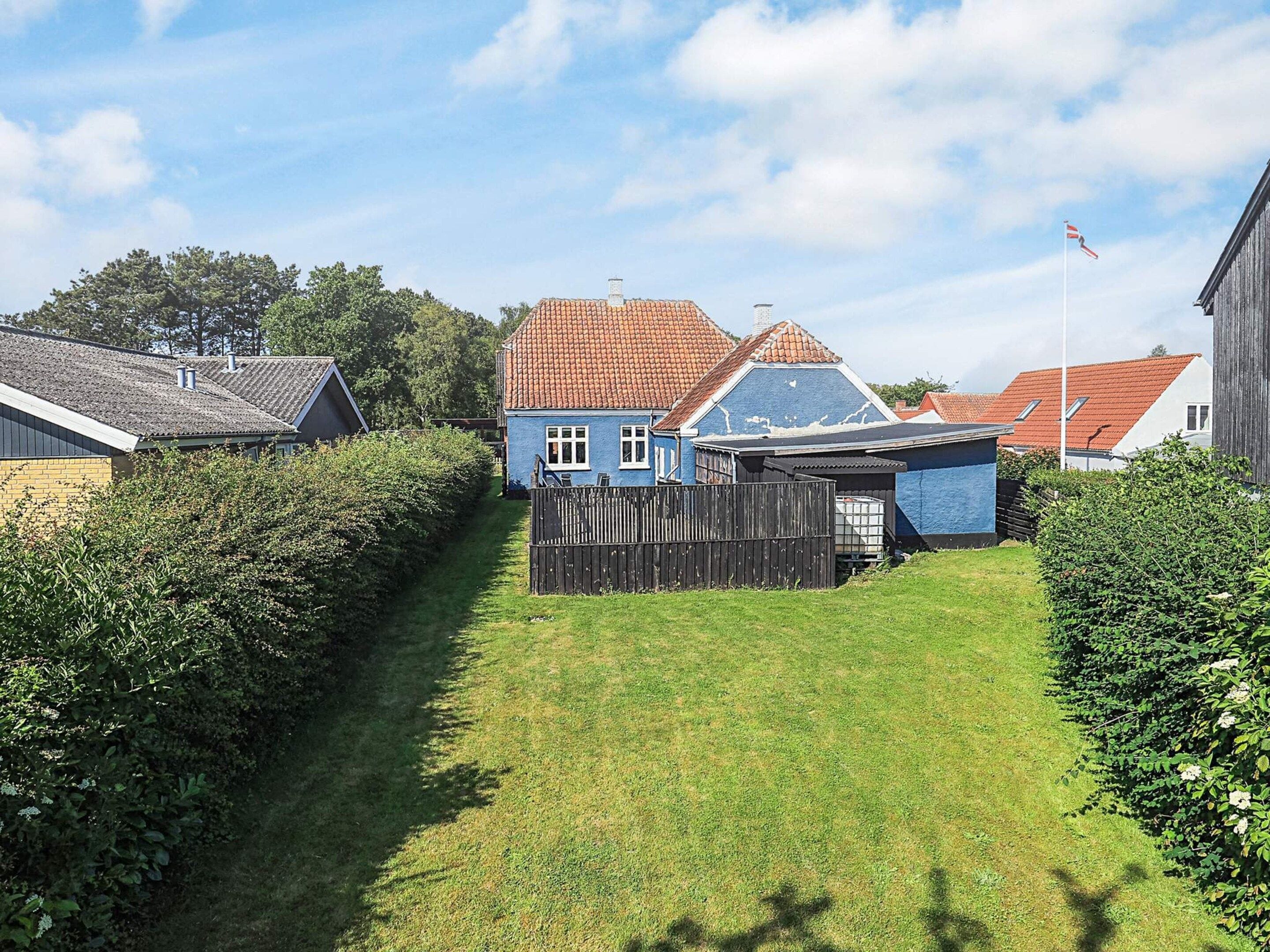 A residential area with a blue house, a wooden fence, and a clear sky.
