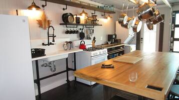 Une cuisine avec un îlot central en bois, des meubles blancs et des ustensiles de cuisine suspendus.