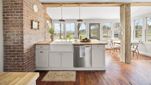 A kitchen with a brick wall, white cabinets, a wooden countertop, and a view of the outdoors. - Farmhouse Retreat, Infrared Sauna, Fire-Pit, Fast Wifi, Golf & 3-Acre Privacy (Valatie)