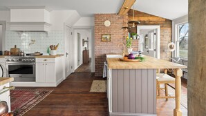 A spacious kitchen with white cabinetry, a wooden island, and a brick accent wall. - Farmhouse Retreat, Infrared Sauna, Fire-Pit, Fast Wifi, Golf & 3-Acre Privacy (Valatie)