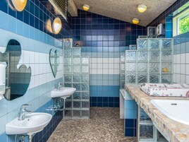 Un baño con azulejos azules y blancos, dos lavamanos, un espejo y una zona de ducha.