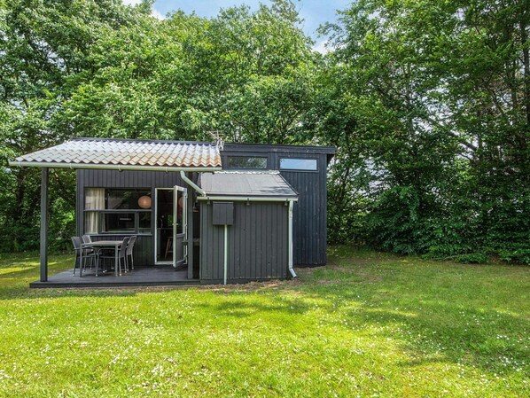A small, dark-colored wooden cabin with a tiled roof and a patio area. - 4 Person Holiday Home in Hampen (Hampen)