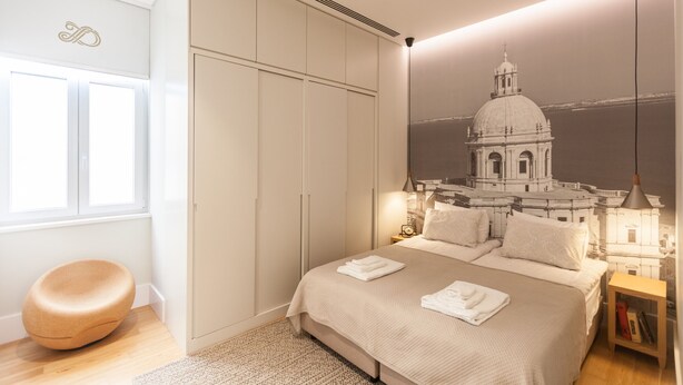 Un dormitorio con una cama grande, un armario, una silla redonda y un mural en la pared con la imagen de un edificio.