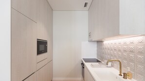 Una cocina moderna con microondas integrado, lavavajillas y un lavamanos con grifo dorado.
