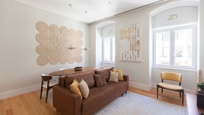 Una sala de estar moderna con un sofá marrón, una mesa redonda y una silla. Se observan obras de arte abstractas en la pared y un gran ventanal con vistas.