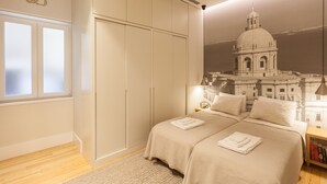 A bedroom with a large wardrobe, a bed with a duvet, and a wall mural of a building.