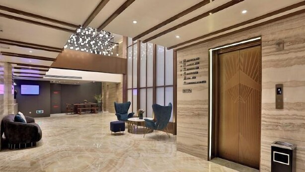 Een moderne lobby met een marmeren vloer, blauwe stoelen, een ronde tafel en een grote kroonluchter.