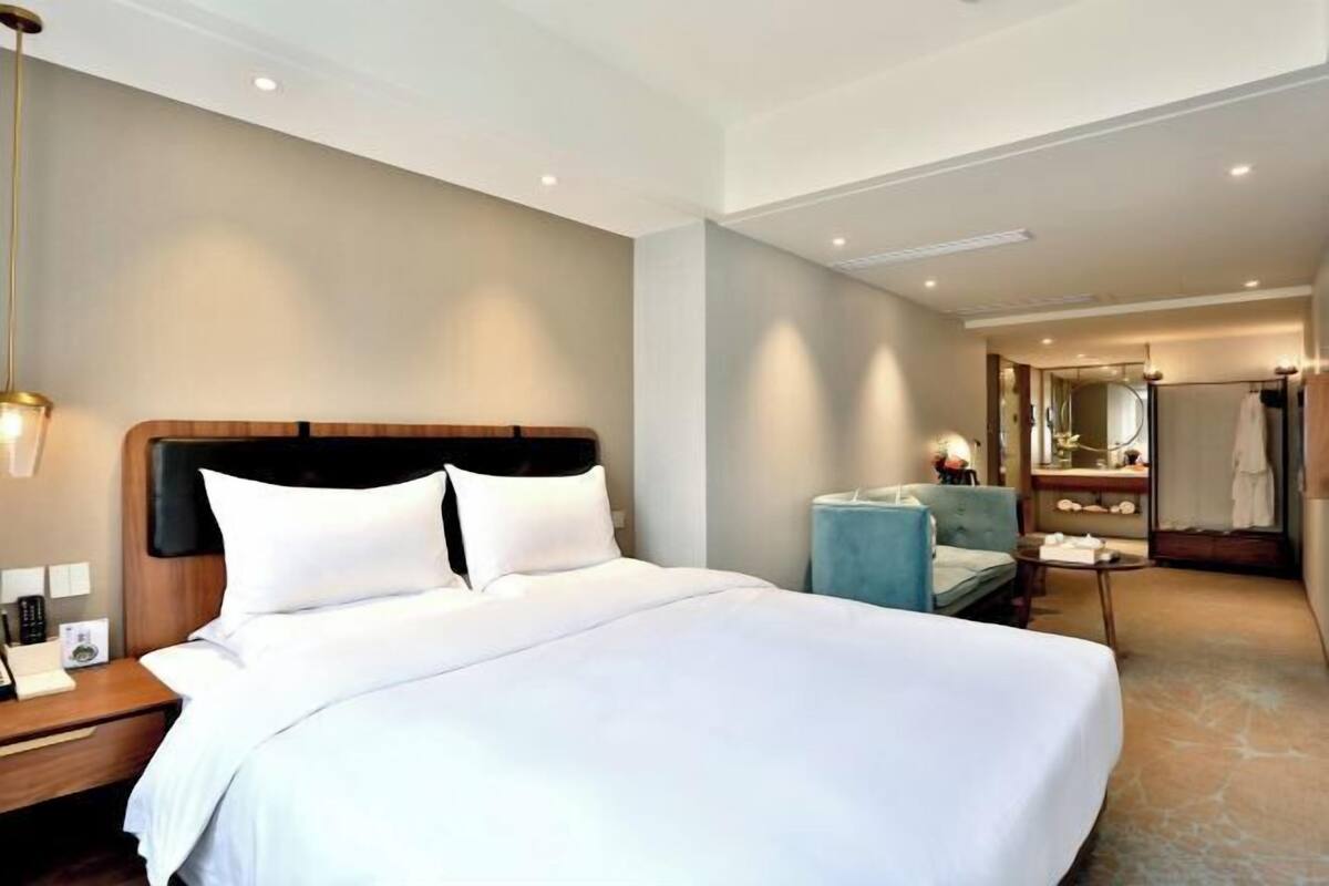 A hotel room with a large bed, bedside table, lamp, and a bathroom with a mirror and towel rack.