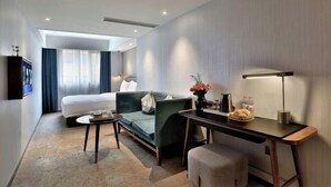 Een moderne hotelkamer met een bed, een groene bank, een bureau en een televisie.