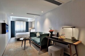 Ein modernes Hotelzimmer mit einem Bett, einem grünen Sofa, einem Schreibtisch und einem Fernseher.