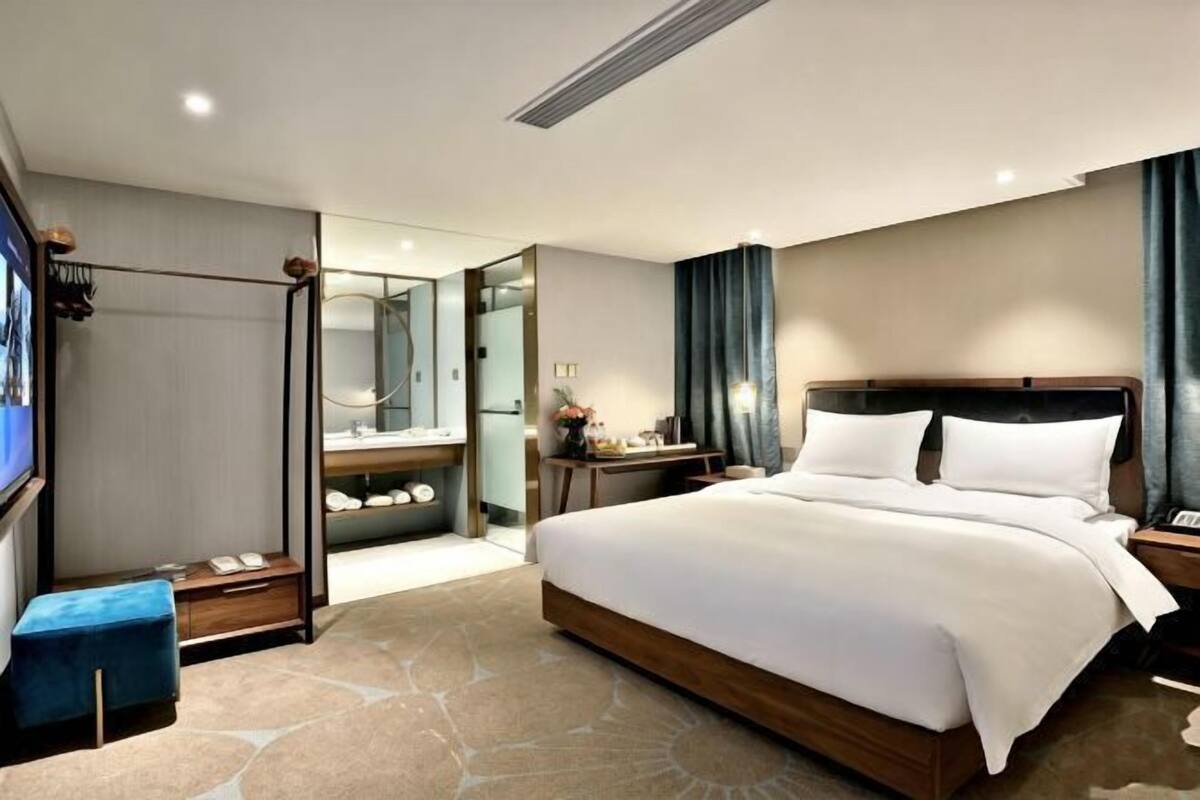 A modern hotel room with a large bed, a desk, a mirror, and a wardrobe.