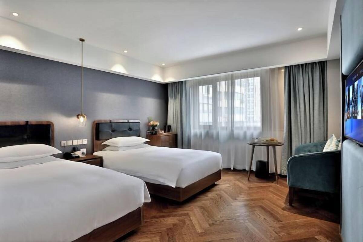 A hotel room with two beds, a TV, a small table, and a chair.