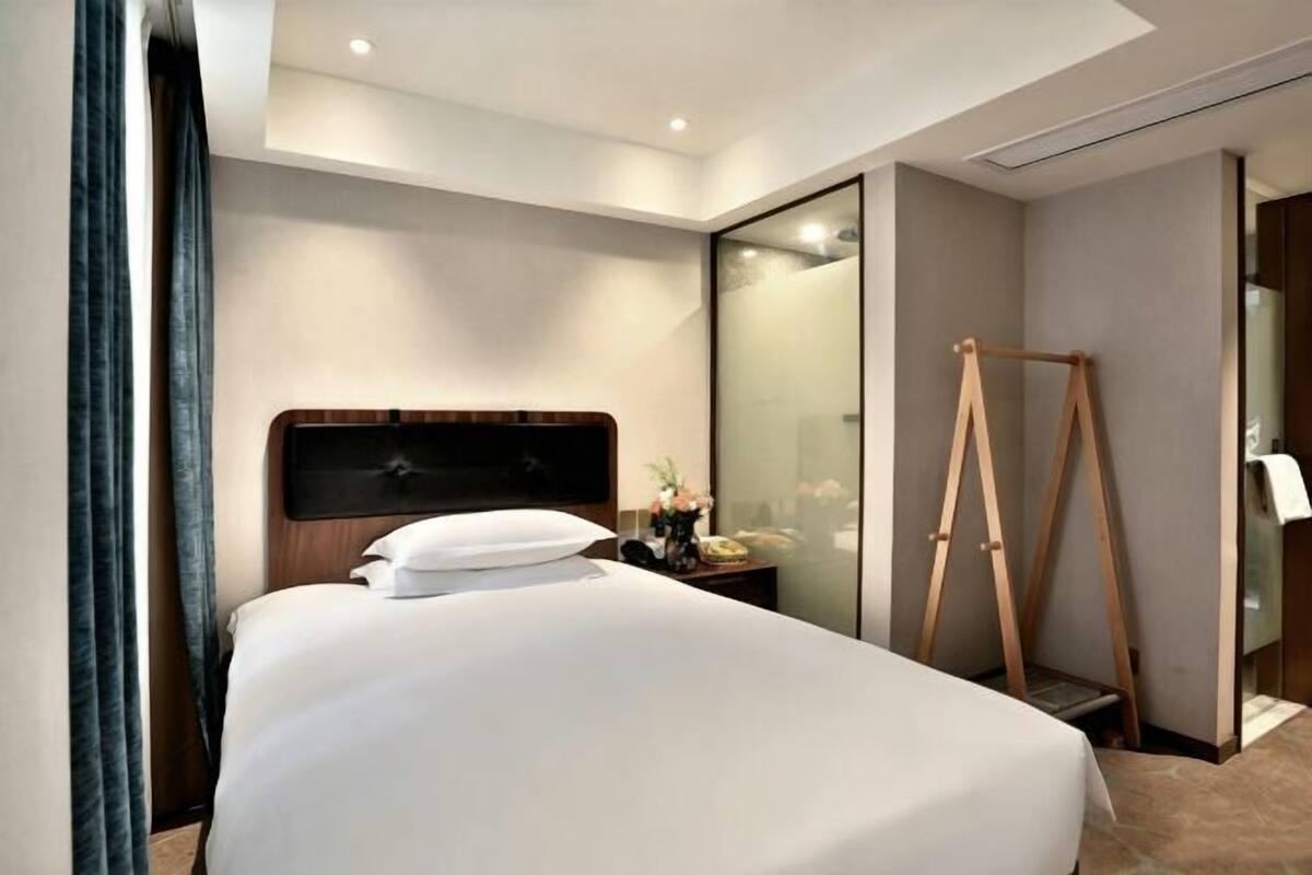 A hotel room with a large bed, a bedside table with a lamp, a mirror, and a wooden easel.