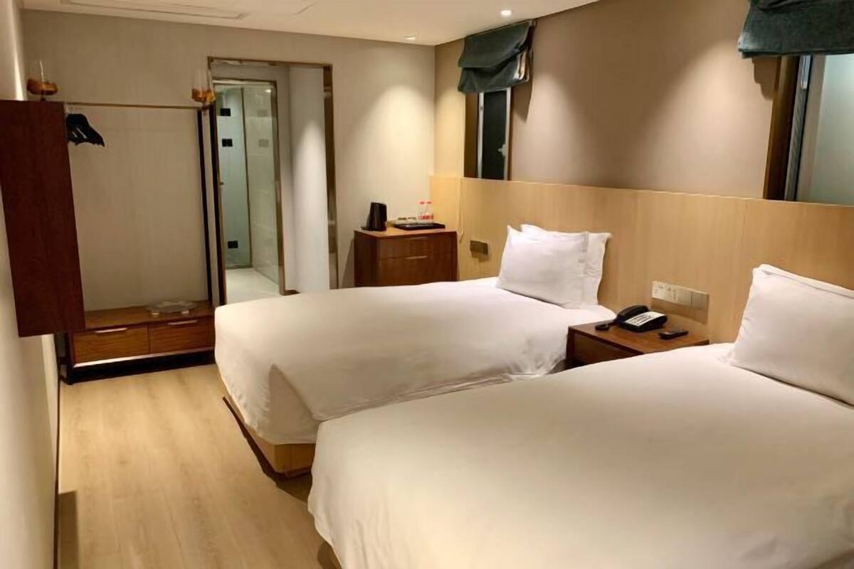 A hotel room with two beds, a wooden headboard, a bedside table with a phone, a mirror, and a wardrobe.